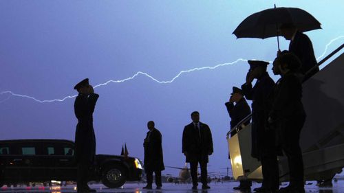Lightning streaks across the sky as President Donald Trump walks from Air Force One carrying an umbrella.