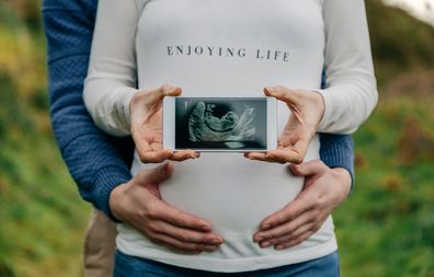 Pregnant woman showing ultrasound of her baby on the mobile embraced by her partner
