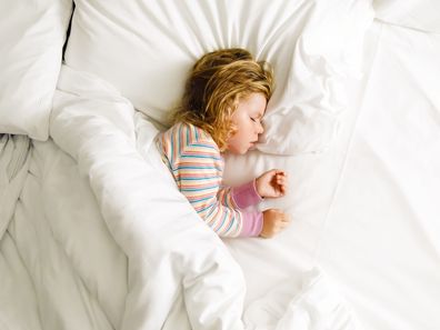 Cute little toddler girl sleeping in big bed of parents. Adorable baby child dreaming in hotel bed on family vacations or at home