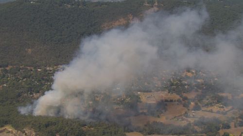 An out-of-control bushfire is burning dangerously close to homes in Melbourne's east as erratic winds and heatwave conditions are felt across the city.