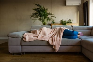 Young woman lying down on sofa in living room covered by blanket.