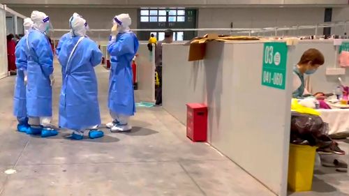 In this image taken from video provided by Beibei, medical workers wearing protective suits chat as a resident takes a rest at the convention centre on April 15, 2022, in Shanghai.