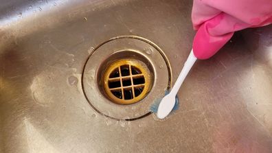 Woman cleans kitchen sink drain hole with a toothbrush