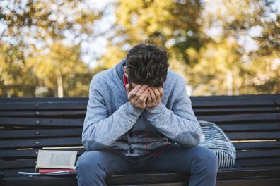 Teenager sits on a bench in the park and listen to music. Sad teenage boy