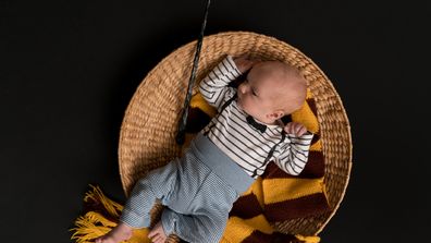 Baby lying in basket with red and yellow scarf and wand.