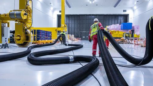 Workers carry exhaust pipes away from the assembly hall. These pipes are used to expel exhaust from trucks that deliver the large components to the clean facility.
