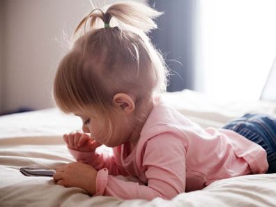 Toddler using a phone while lying on her stomach in bed