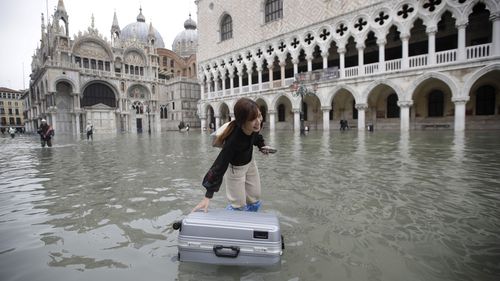 A tourist pushes her floating luggage in an inundated St. Mark's Square during the floods of 2019.