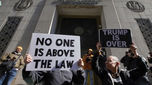 People hold up posters as part of a protest in front of the courthouse ahead of former President Donald Trump's anticipated indictment on Monday, March 20, 2023, in New York.