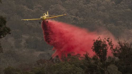 A small aircraft dumps fire retardant behind houses at the foot of Mount Tennant as the fire front of the Orroral Valley fire creeps through the Namadgi National Park on January 30, 2020 in Canberra.