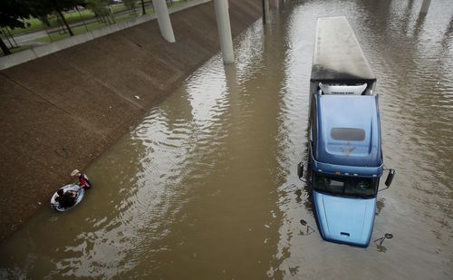 An unidentified man helps Carlos Torres, in tube, get to dry ground after Torres drove his tractor-trailer into a freeway flooded by Hurricane Harvey. (AAP)