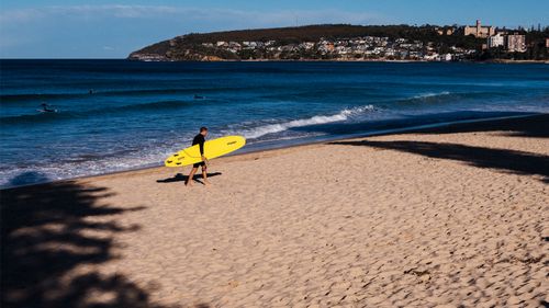 A lone surfer walks across Manly Beach, as the lockdown in Sydney edges closer to its fifth week.