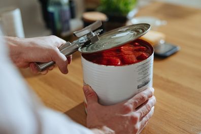 High angle view of an anonymous chef making a healthy meal with canned tomato In the kitchen.