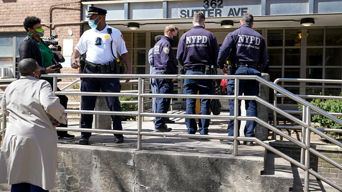 Police officers and community leaders stand outside the building where a man shot the mother of his child and two of her daughters dead before turning the gun on himself, Tuesday, April 6, 2021, in the Brownsville neighborhood of the Brooklyn borough of New York. 