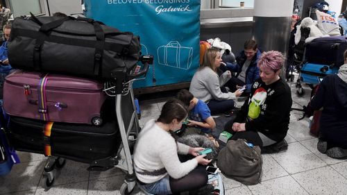 People sit on the ground beside their luggage inside Gatwick Airport.