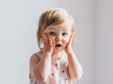 Surprised shocked child toddler girl with hands on her cheeks isolated on light background