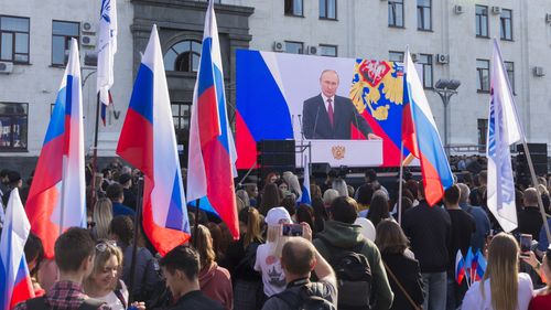 People with Russian national flags watch Russian President Vladimir Putin's address as they gather during celebrations marking the incorporation of the Luhansk region into Russia in Luhansk, Ukraine, Friday, Sept. 30, 2022.