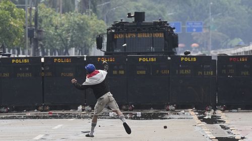 Um manifestante joga uma pedra na polícia durante um protesto contra os luxuosos subsídios concedidos aos membros do Parlamento, fora do Parlamento em Jacarta, Indonésia, domingo, 31 de agosto de 2025. (AP Photo/Dita Alangkara)