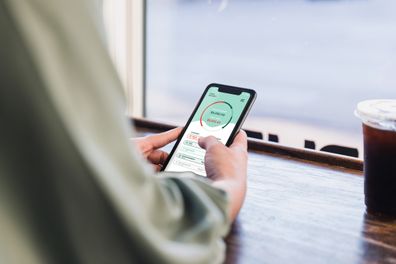 While sitting in a coffee shop, an unrecognizable woman uses a banking app. She is checking her account balance.