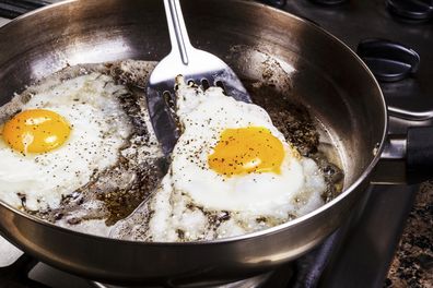 Eggs in frying pan being cooked by bacon grease with spatula