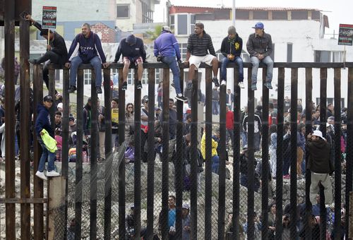 The refugees sit on top of the border wall on the beach during a gathering of migrants living on both sides of the border. (AAP)