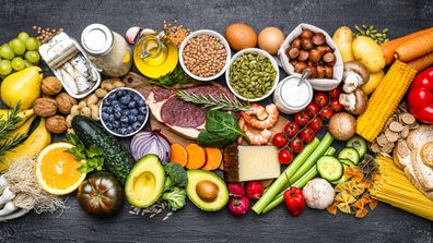 Overhead view of a large group of healthy food for a well balanced diet arranged side by side on black background.