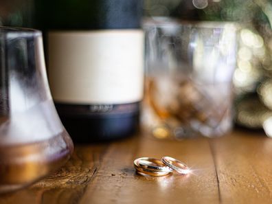 Wedding rings on a rustic wooden table with scotch and champagne in the background, out of focus.  Negative space for text or copy space,