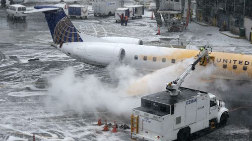 A man de-ices a plane during a light snow at a gate at LaGuardia Airport in New York, (AAP)