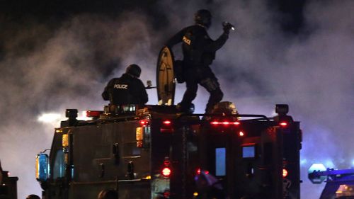 A police officer is about to throw a tear gas canister as police try to disperse demonstrators who are protesting the shooting death of Michael Brown in Ferguson, Missouri. (AAP)