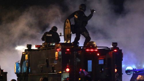 An officer throws a tear gas canister as police try to disperse demonstrators. (AAP)