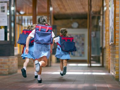 Rear view of excited students running towards entrance. Girls are carrying backpacks while leaving from school. Happy friends are wearing school uniforms.