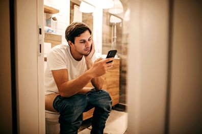 Man sitting on toilet and using smart phone