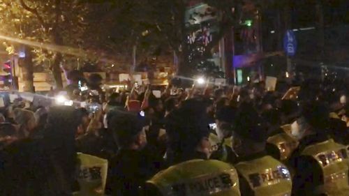 In this image from video obtained by The Associated Press, police, foreground, watch protesters in Shanghai on Saturday, Nov. 26, 2022. Protests against Chinas restrictive COVID measures appeared in a number of cities Saturday night, in displays of public defiance fanned by anger over a deadly fire in the western Xinjiang region.