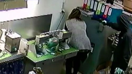 A masked offender holds a female staff member at gunpoint. (9NEWS)