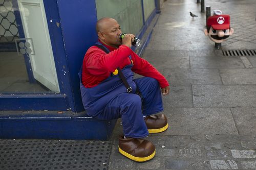A man wearing a Mario Bros costume takes a break from work posing for tourist photos in the shade at Sol square in Madrid, Spain.