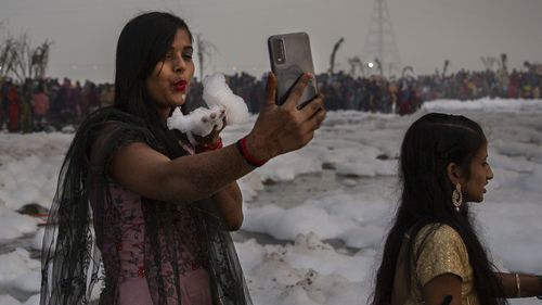 A Hindu devotee takes a selfie while holding handful of chemical foam she picked from Yamuna river during Chhath Puja festival in New Delhi, India, Wednesday, Nov. 10, 2021. A vast stretch of one of India's most sacred rivers, the Yamuna, is covered with toxic foam, caused partly by high pollutants discharged from industries ringing the capital New Delhi. Still, hundreds of Hindu devotees Wednesday stood knee-deep in its frothy, toxic waters, sometimes even immersing themselves in the river for 