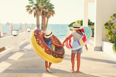 Two small girls with inflatable toys on the beach. Summer vacation and traveling concept