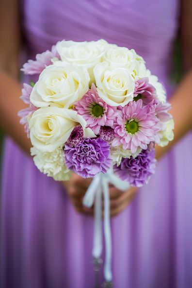 Bridesmaid holding bouquet with white, purple, and lavender flowers.