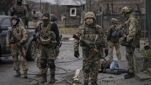 Украинские солдаты стоят вокруг тела мужчины в штатском в оккупированном Россией пригороде Киева Буча. 