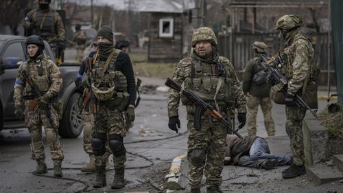 Des militaires ukrainiens entourent le corps d'un homme vêtu de vêtements civils, dans la banlieue de Bucha, anciennement occupée par la Russie. 