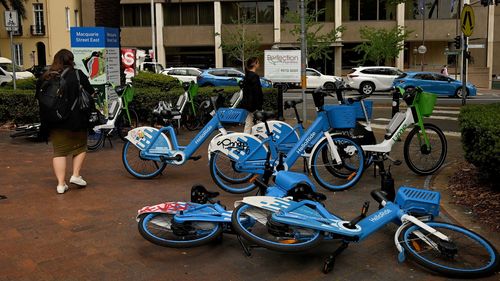 I pedoni passano davanti alle biciclette elettriche vicino alla Biblioteca di Stato del NSW a Sydney.