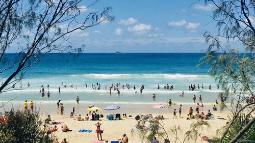 Horizontal Seascape of people enjoying the summer sun on busy tourist beach holiday with sand turquoise waves blue sky at famous surf ocean Byron Bay Australia