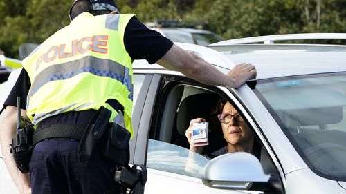 A motorist shows identifcation at a checkpoint on the Gold Coast Highway at Coolangatta on the Queensland/NSW  border , Thursday, March 26, 2020.