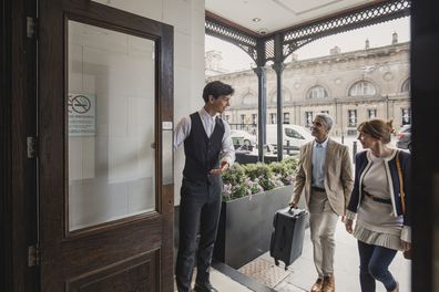 Hotel doorman welcomes an adult couple for a weekend getaway.