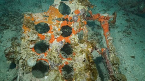 The punched holes of the split-panel dive brakes from an SBD-5 Dauntless dive bomber are visible resting on the floor of the lagoon near the main debris site.