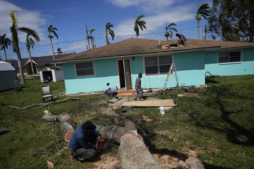 Członkowie rodziny pracują razem, aby naprawić dom po upadku gałęzi drzewa, uszkadzając dach, w Fort Myers na Florydzie, czwartek, 29 września 2022 r.