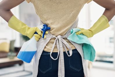 Photo of unrecognizable woman using rubber gloves and sanitizer to clean her house