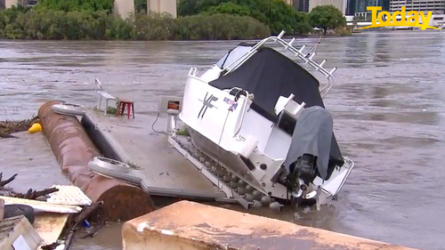 A small boat lies washed up along the banks of the Brisbane river.