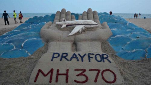 Beachgoers walk past a sand sculpture made by Indian sand artist Sudersan Pattnaik with a message of prayers for the missing Malaysian Airlines flight. (Getty)