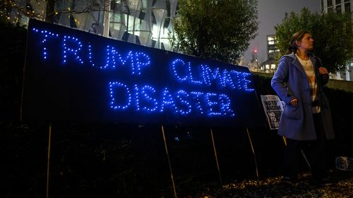 A woman stands next to a banner reading "Trump Climate Disaster" as a small group of protesters hold a protest against the new Trump presidency 